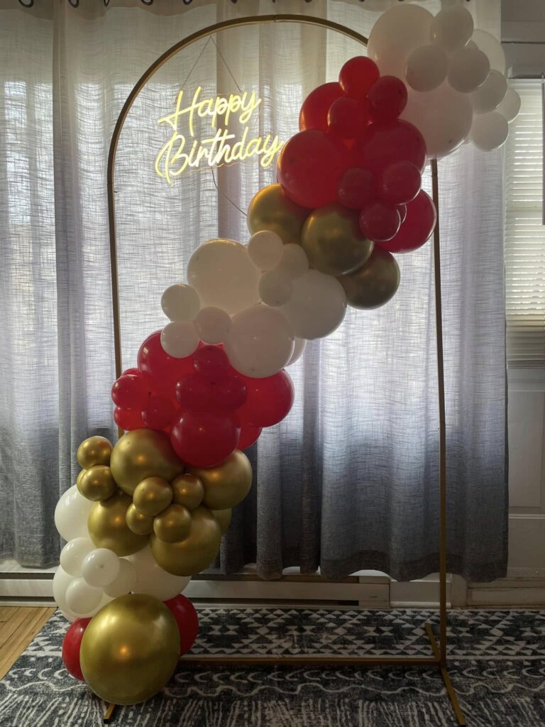 Elegant Happy Birthday backdrop in Montreal featuring a vibrant red, white, and gold organic balloon garland and custom arched signage for a festive milestone celebration.