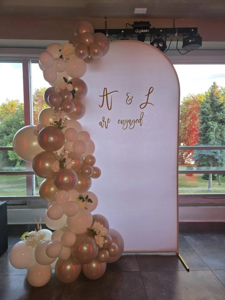 Custom engagement party backdrop in Montreal featuring white and metallic gold balloon clusters and "A & L are engaged" personalization for an elegant indoor celebration.