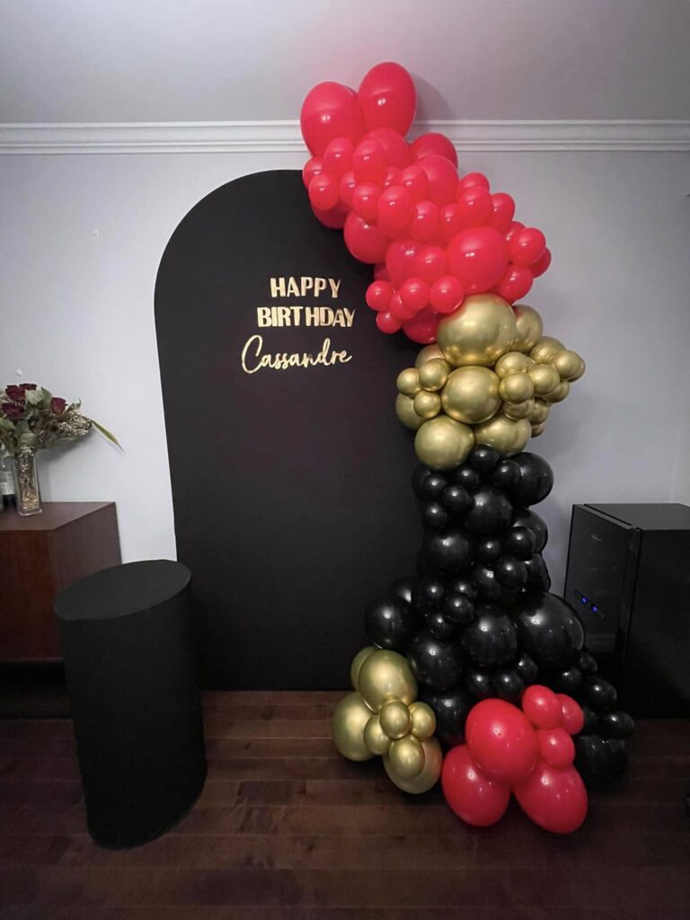 Bold red, gold, and black organic balloon installation with a matte black "Happy Birthday" backdrop for a luxury milestone event in Montreal.