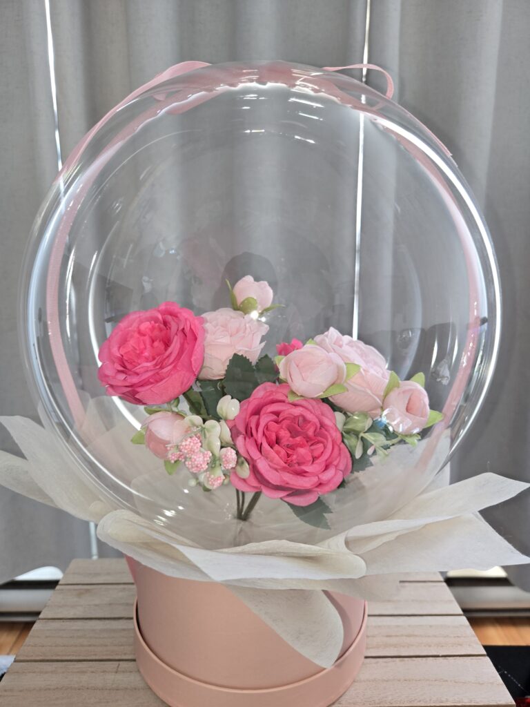 Elegant pink and blush rose bouquet encased in a clear Bobo balloon, presented in a soft pink signature gift box with white tissue paper accents by La Balloonerie Montreal.