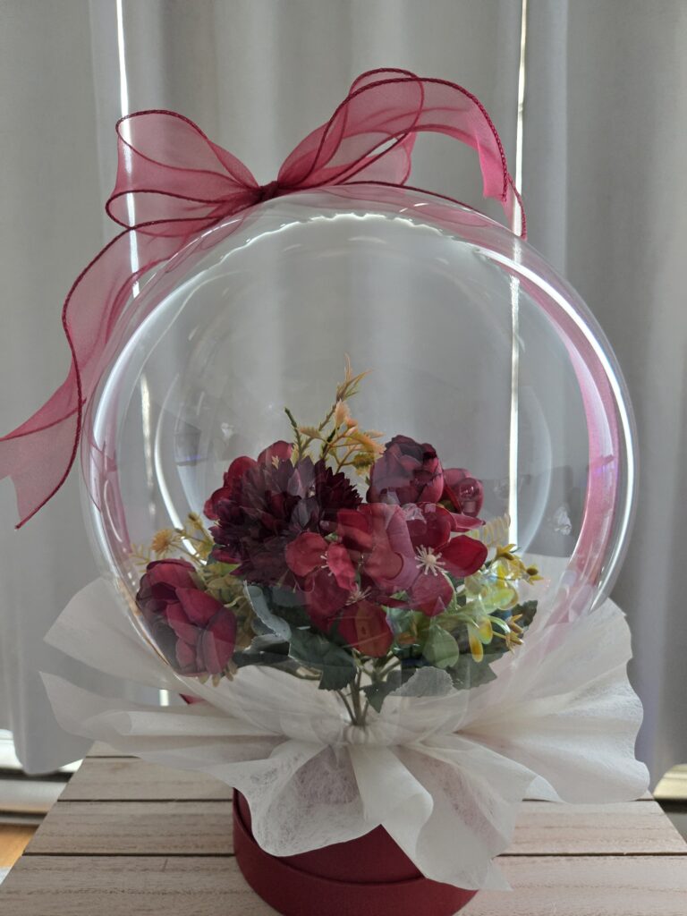 Luxe Bobo signature flower box in Montreal featuring a romantic arrangement of rich red blooms and greenery encased in a clear artisan globe with a satin red bow.