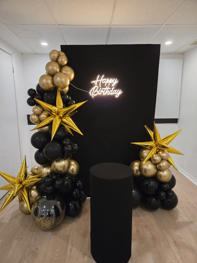 Luxe black and gold birthday backdrop in Montreal featuring a "Happy Birthday" neon sign, organic balloon clusters, and metallic gold star accents for a high-end celebration.