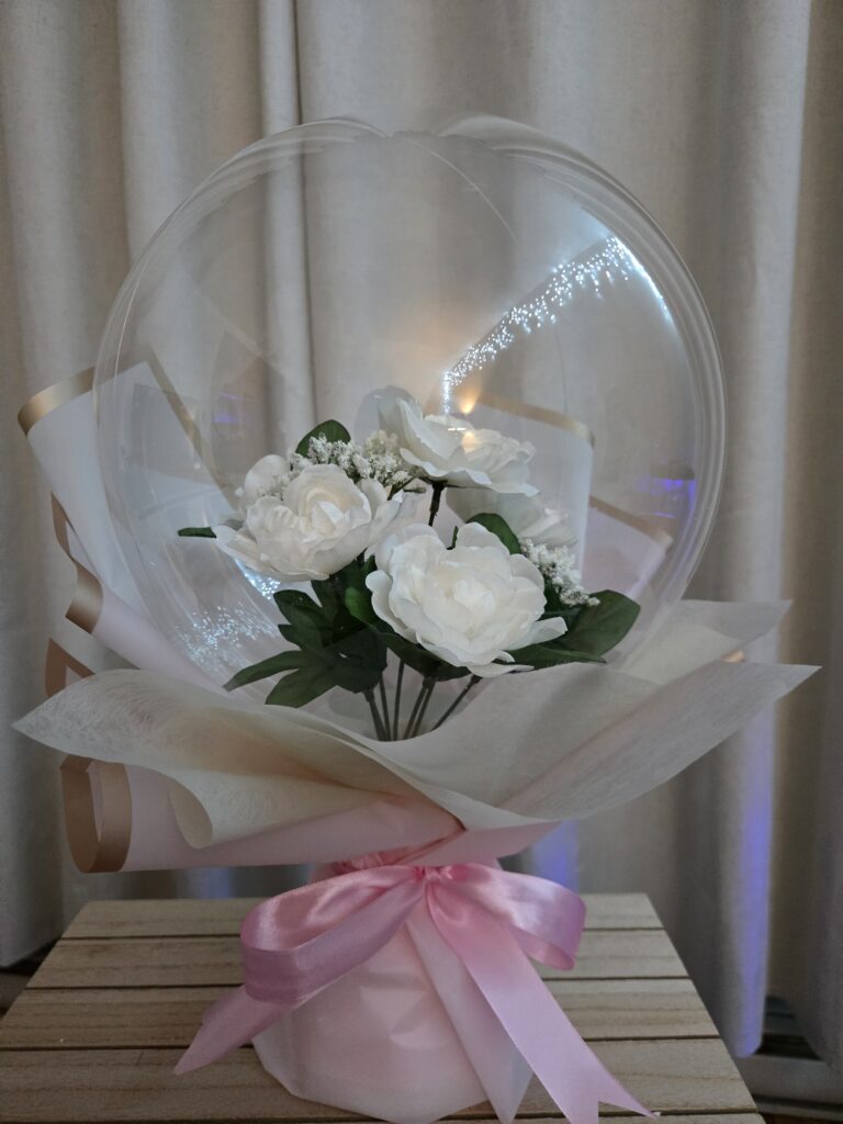 Minimalist white rose Bobo balloon bouquet wrapped in premium cream paper with a soft pink ribbon, perfect for Montreal weddings, baptisms, or elegant celebrations.
